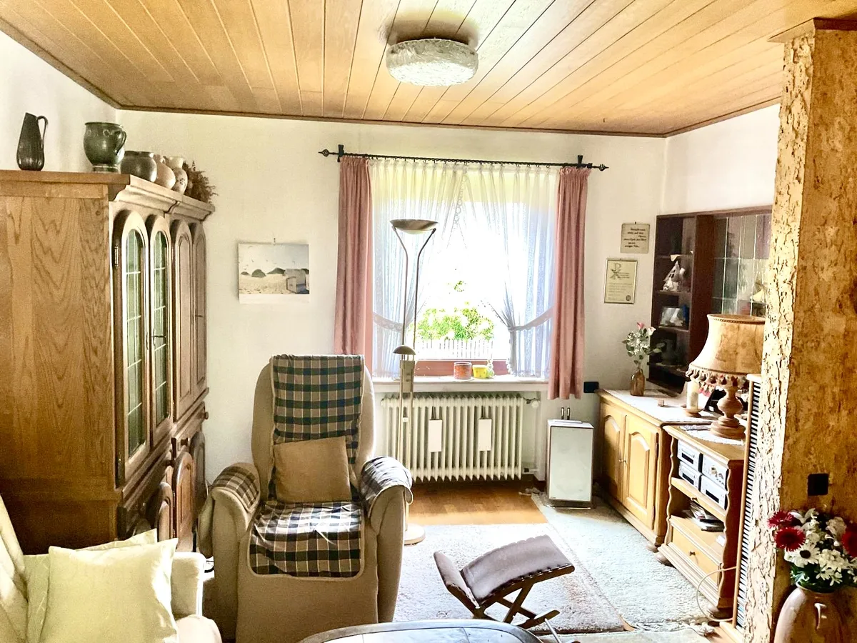 Wohnzimmer im Ausgangszustand: Eichenschrankwand, Sessel mit Decke, Gardinen und viele persönliche Dinge